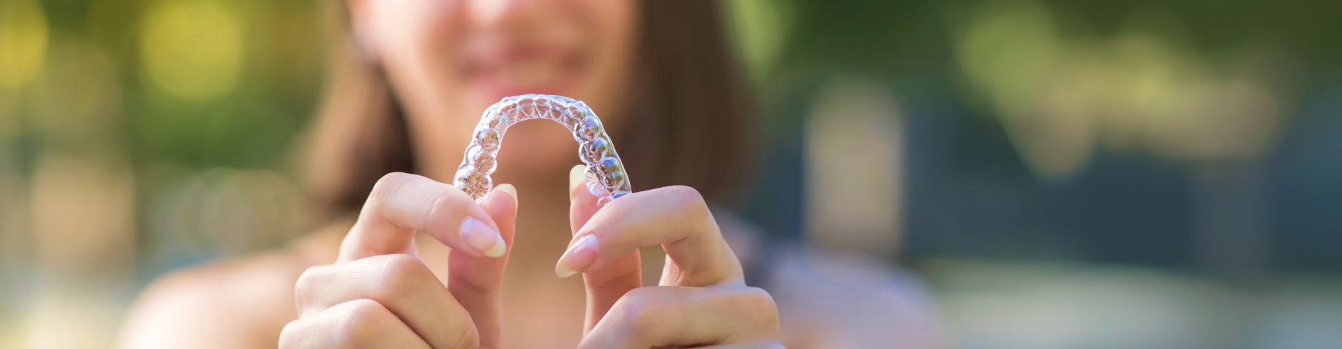 Patient holding a clear Invisalign aligner with both hands.
